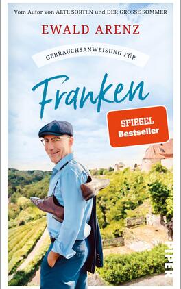 Gebrauchsanweisung für Franken Das Buchcover zeigt einen lächelnden Mann mit Brille und Kappen im Vordergrund, der eine braune Tasche in der Hand hält. Im Hintergrund erstreckt sich eine malerische Landschaft mit Weinbergen und sanften Hügeln. Der Titel „Gebrauchsanweisung für Franken“ steht in geschwungener blauer Schrift, während der Hinweis „SPIEGEL Bestseller“ in einem rot umrandeten Quadrat hervorgehoben ist. Der Autorennamen „Ewald Arenz“ ist oben auf dem Cover platziert. Die Atmosphäre vermittelt eine einladende und freundliche Stimmung.