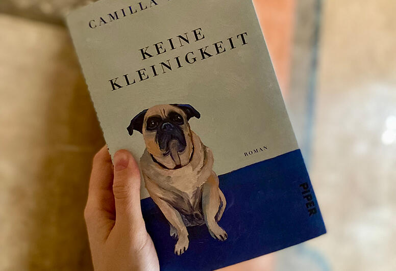 Eine Hand hält ein Buchcover. Der Titel lautet 'Keine Kleinigkeit' von Camilla Barnes. Auf dem Cover ist ein sitzender Hund abgebildet.