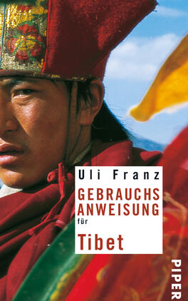 Gebrauchsanweisung für Tibet Das Buchcover zeigt einen nahen Blick auf einen jungen Mann, der traditionelle tibetische Kleidung trägt. Sein Gesichtsausdruck ist ernst und nachdenklich. Die Farben des Covers sind lebhaft, mit einem dominierenden Rot und Gelb, die die Symbolik der tibetischen Kultur unterstreichen. Der Titel „GEBRAUCHSANWEISUNG für Tibet“ ist in großer, schwarzer Schrift auf hellem Hintergrund platziert, darunter steht der Name des Autors „Uli Franz“. Der Hintergrund zeigt einen klaren blauen Himmel, der eine weite, offene Atmosphäre vermittelt.