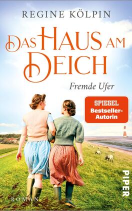 Das Haus am Deich – Fremde Ufer Das Buchcover zeigt zwei Frauen, die Hand in Hand an einem Deich entlanggehen. Die eine trägt ein hellblaues, die andere ein rotes Kleid. Im Hintergrund erstreckt sich eine Hügel- und Landschaftsrichtung mit Schafen und einem Leuchtturm. Der Himmel ist blau mit weißen Wolken, was eine freundliche Atmosphäre vermittelt. Der Titel „Das HAUS am DEICH“ ist groß und orange gehalten, ergänzt durch den Untertitel „Fremde Ufer“. Unten rechts steht „SPIEGEL Bestseller-Autorin“ in einem roten Feld. Der Verlag ist in der unteren rechten Ecke abgedruckt.