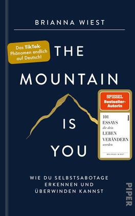 The Mountain Is You Das Buchcover zeigt einen dunkelblauen Hintergrund mit einer minimalistischen, hellgelben Bergsilhouette in der Mitte. Der Titel „THE MOUNTAIN IS YOU“ ist in großen, weißen Buchstaben hervorgehoben. Oben links befindet sich ein gelbes Banner mit dem Text „Das TikTok-Phänomen endlich auf Deutsch!“. Auf der rechten Seite ist ein rotes Rechteck mit dem Hinweis „SPIEGEL Bestseller-Autorin“ und dem Namen „Brianna Wiest“. Darunter steht in kleinerer Schrift „WIE DU SELBSTABENTAGE ERKENNEN UND ÜBERWINDEN KANNST“. Die Atmosphäre ist inspirierend und motivierend.