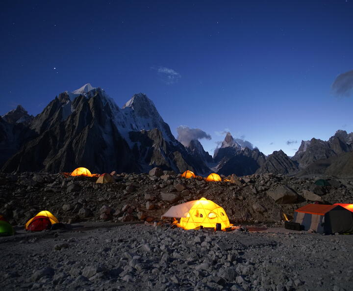 Beleuchtete Zelte vor Bergkette in der Dämmerung