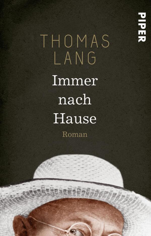 Das Buchcover zeigt einen dunkelgrauen Hintergrund, der die zentrale Figur in einem weißen Hut umgibt. Der Name des Autors, „THOMAS LANG“, ist in einer eleganten, goldenen Schrift oben platziert. Darunter steht der Titel „Immer nach Hause“ in einer klaren, weißen Schriftart. Am unteren Rand des Covers ist das Wort „Roman“ in einer kleineren Schriftgröße zu sehen. Die Atmosphäre des Covers wirkt sowohl nachdenklich als auch einladend.