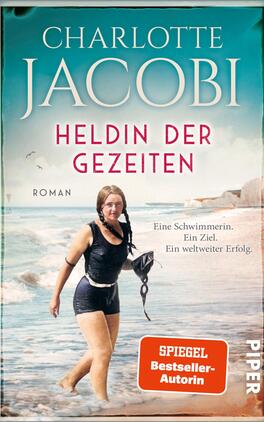 Heldin der Gezeiten – Eine Schwimmerin. Ein Ziel. Ein weltweiter Erfolg. Das Buchcover zeigt eine Schwimmerin in einem Strandsetting, die entschlossen im Wasser steht. Der Hintergrund ist in sanften Blautönen gehalten und erzeugt eine ruhige Atmosphäre. Der Titel „Heldin der Gezeiten“ ist in großen, auffälligen roten Buchstaben mittig platziert, während der Autorenname „Charlotte Jacobi“ oben in eleganter Serifenschrift steht. Unter dem Titel befindet sich der Untertitel „Roman“ in kleinerer Schrift. Unten rechts ist der Hinweis „SPIEGEL Bestseller-Autorin“ in einem vertikalen Banner abgebildet.