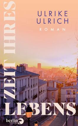 Zeit ihres Lebens Das Buchcover zeigt eine stimmungsvolle Stadtansicht bei Sonnenuntergang. Im Vordergrund sind elegante, hellbeige Gebäude und eine gepflasterte Straße zu sehen. Der Himmel ist in sanften Orangetönen gefärbt. Der Titel „ZEIT IHRES LEBENS“ ist groß und in verspielter Schriftart am linken Rand angeordnet, während der Name der Autorin „ULRIKE ULRICH“ in deutlich lesbarer blauer Schrift darüber platziert ist. Darunter steht das Wort „Roman“ in kleinerer Schrift.