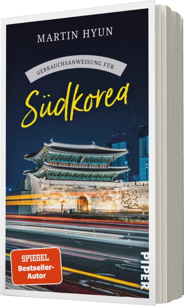 Das Buchcover zeigt eine beeindruckende Nachtaufnahme eines traditionellen südkoreanischen Gebäudes mit Ziegeldach, beleuchtet von Straßenlichtern. Der Hintergrund ist urban und modern, mit Wolkenkratzern und einer leicht verschwommenen Verkehrsszene. Der Titel „Gebrauchsanweisung für Südkorea“ ist in lebhaftem Gelb hervorgehoben, während der Autor „Martin Hyun“ in einer klaren, weißen Schrift darüber steht. Unten links befindet sich ein rotes Feld mit dem Hinweis „SPIEGEL Bestseller-Autor“ und dem Verlagsnamen „PIPER“ in kleinerer Schrift.