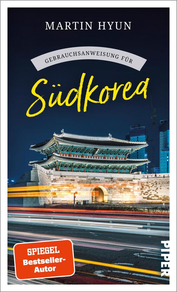 Das Buchcover zeigt eine nächtliche Ansicht des Dongdaemun-Tor in Seoul, umgeben von modernen Gebäuden und Lichtern, die eine dynamische Atmosphäre erzeugen. Der Titel „Gebrauchsanweisung für Südkorea“ ist in gelber Schrift in einer handschriftlichen Typografie hervorgehoben, während der Autor „Martin Hyun“ in auffälligem Schwarz oben platziert ist. Unten links befindet sich ein rotes Label mit dem Text „SPIEGEL Bestseller-Autor“. Die Gestaltung vermittelt eine Mischung aus traditioneller und moderner koreanischer Kultur.