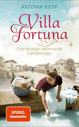 Villa Fortuna Das Buchcover zeigt eine historische Szenerie mit einer Waschküche am Wasser. Im Vordergrund steht eine Frau in traditioneller Kleidung, die Wäsche aus einem Korb wäscht. Die Farbpalette umfasst sanfte Blau- und Erdtöne, die eine nostalgische Atmosphäre vermitteln. Der Titel „Villa Fortuna“ ist in geschwungener, roter Schrift platziert, während darunter der Untertitel „Eine deutsch-italienische Familiensaga“ in schlichterer Schrift zu sehen ist. Das Cover trägt das Branding „SPIEGEL Bestseller“ in einem roten Kästchen.