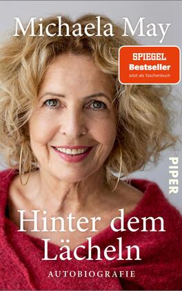 Hinter dem Lächeln Das Buchcover zeigt ein Portrait von Michaela May mit lockigem, blonden Haar und einem warmen Lächeln. Der Hintergrund ist hell und freundlich. Oben links steht der Name „Michaela May“ in großer, eleganter Schrift. Darunter ist der Titel „Hinter dem Lächeln“ in auffälliger roter Schrift, gefolgt von dem Zusatz „AUTOBIOGRAPHIE“ in kleinerer Schrift. Oben rechts befindet sich ein rotes Label mit der Aufschrift „SPIEGEL Bestseller“, ergänzt durch den Hinweis „Jetzt als Taschenbuch“.