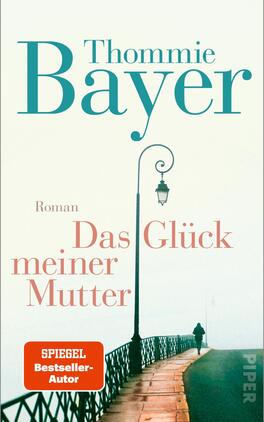 Das Glück meiner Mutter Das Buchcover zeigt eine melancholische, neblige Straßenszene mit einem Gehweg und einer kunstvollen Eisenbahnbrücke im Vordergrund. Ein einzelner Mensch geht in die Ferne, während eine Straßenlaterne sanft beleuchtet. Die Farbpalette ist in sanften Blau- und Rosatönen gehalten. Der Titel „Das Glück meiner Mutter“ erscheint in kräftigem Orange, der Schriftzug ist hervorstechend. Der Autorname „Thommie Bayer“ hebt sich in elegantem Türkis ab. Oben links ist der Hinweis „SPIEGEL Bestseller-Autor“ in einer orangefarbenen Box platziert.