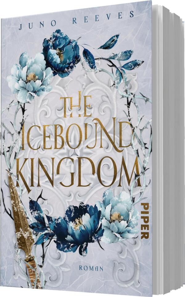 Das Buchcover zeigt eine elegante, frostig anmutende Gestaltung mit einem zentralen, kunstvollen Blumendesign in Blau und Weiß. Der Titel „THE ICEBORN KINGDOM“ ist in großem, goldenen Schriftzug platziert, wodurch er sich markant abhebt. Im Hintergrund sind filigrane, weiße Muster zu erkennen, die eine mystische Atmosphäre schaffen. Der Name der Autorin „Juno Reeves“ ist dezent oben auf dem Cover angebracht. In der unteren Ecke befindet sich der Verweis auf den Verlag „PIPER“ sowie das Wort „Roman“.