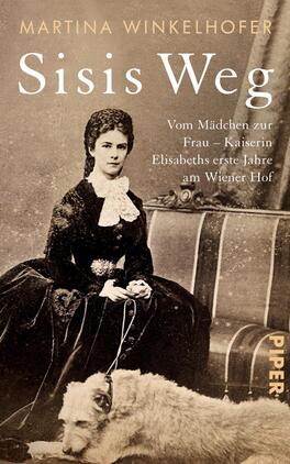 Sisis Weg Das Buchcover zeigt eine historische Schwarz-Weiß-Fotografie einer jungen Frau in einem eleganten Kleid, die vor einem mit Stoff bezogenen Sofa sitzt. Ihr Blick ist nachdenklich und selbstbewusst. Der Titel „Sisis Weg“ ist in goldener, eleganter Schrift am oberen Rand platziert, während der Untertitel „Vom Mädchen zur Frau – Kaiserin Elisabeths erste Jahre am Wiener Hof“ darunter in kleinerer Schrift steht. Am unteren Rand befindet sich das Verlagslogo in dezentem Design. Eine freundliche, nostalgische Atmosphäre wird durch die Darstellung und die Farbtöne vermittelt.