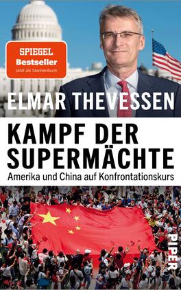 Kampf der Supermächte Das Buchcover zeigt den Autor Elmar Thevessen vor einer Kulisse des US-Kapitols, umrahmt von einer amerikanischen Flagge. Der Titel „Kampf der Supermächte“ ist in großen, schwarzen Buchstaben auf weißem Hintergrund platziert. Darunter steht der Untertitel „Amerika und China auf Konfrontationskurs“ in kleinerer Schrift. Im unteren Teil des Covers ist eine Menschenmenge mit einer roten Flagge und einer Gelben Stern, was die Thematik des Buches unterstreicht. In der oberen linken Ecke befindet sich ein orangefarbenes Label mit dem Hinweis „SPIEGEL Bestseller – Jetzt als Taschenbuch“.